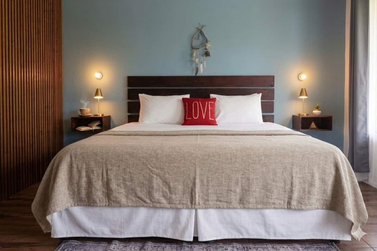 A neatly made bed with a red pillow, two bedside lamps, and a wall-mounted dreamcatcher.