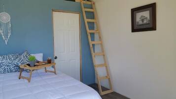 Un dormitorio con una cama, una escalera, una puerta, un cuadro enmarcado y un atrapasueños en la pared.