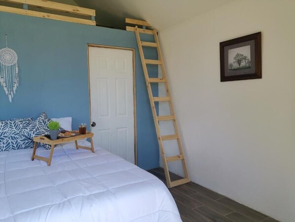 Quarto com cama, escada, porta, quadro e um apanhador de sonhos na parede.