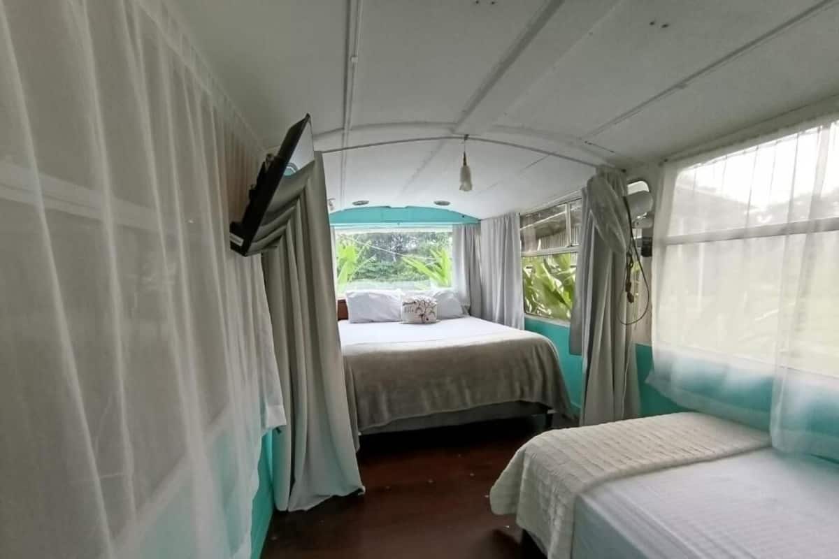 A room with a bed, a window with curtains, and a view of greenery outside.