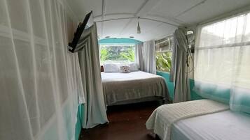 A room with a bed, a window with curtains, and a view of greenery outside.