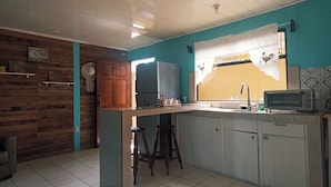 A kitchen with a wooden wall, a teal accent wall, a tiled floor, and a window with a curtain. - The Dreamcatcher House (San Pedro)