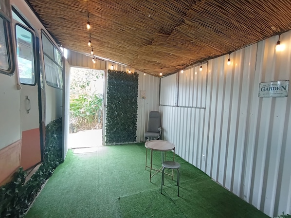 A room with a green artificial turf floor, a chair, a small table, a wall with vertical stripes, and a sign that reads 'To Plant A GARDEN'.