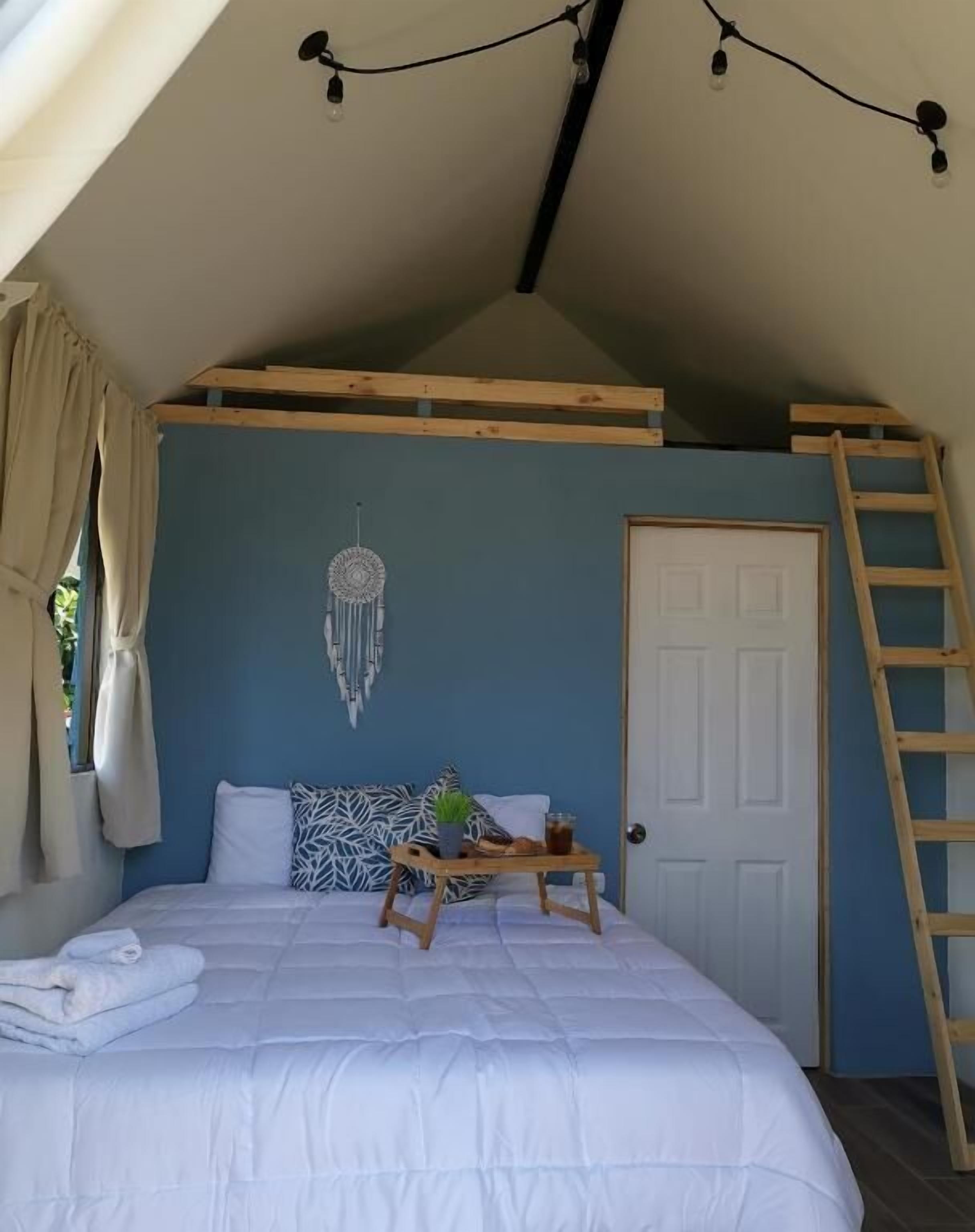 Een slaapkamer met een stapelbed, een nachtkastje met dienblad, een dromenvanger, een ladder en een deur.