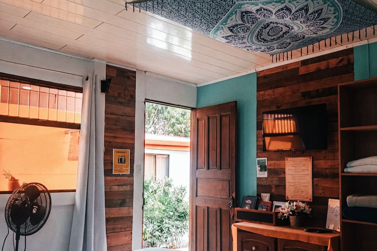 A bedroom with a bed, a desk, a wardrobe, and a ceiling fan.