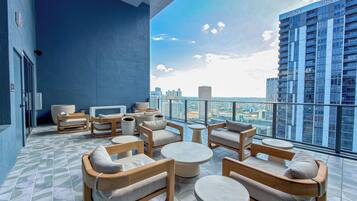 A balcony with seating, a large window, and a city view.