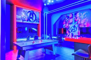 A room with a foosball table, a large wall mural, and a desk with a computer.