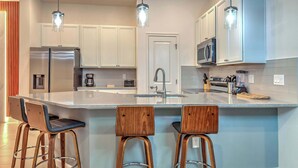 A modern kitchen with a central island, stainless steel appliances, and wooden bar stools. - Luxury Townhouse w/ Private Pool Near Disney & Universal (Orlando)
