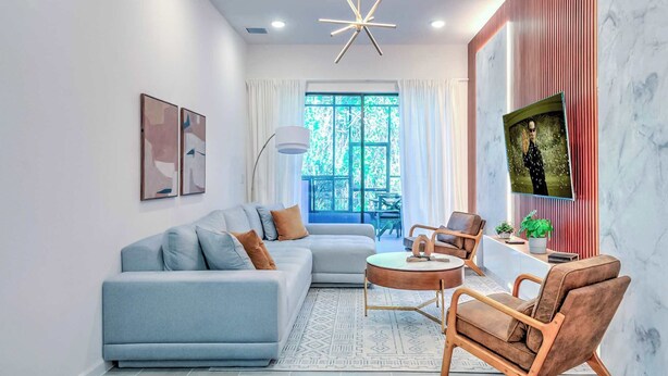 A modern living room with a sectional sofa, a round coffee table, a wooden chair, and a TV mounted on the wall. - Luxury Townhouse w/ Private Pool Near Disney & Universal (Orlando)