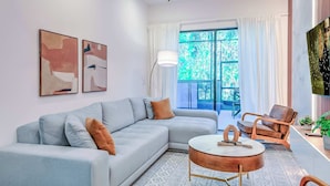 A modern living room with a sectional sofa, a round coffee table, a wooden chair, and a large window with curtains. - Luxury Townhouse w/ Private Pool Near Disney & Universal (Orlando)