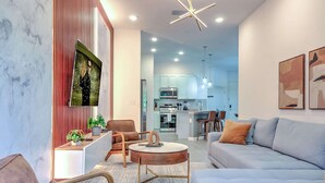 A modern living room with a sofa, chairs, a coffee table, and a kitchen in the background. - Luxury Townhouse w/ Private Pool Near Disney & Universal (Orlando)