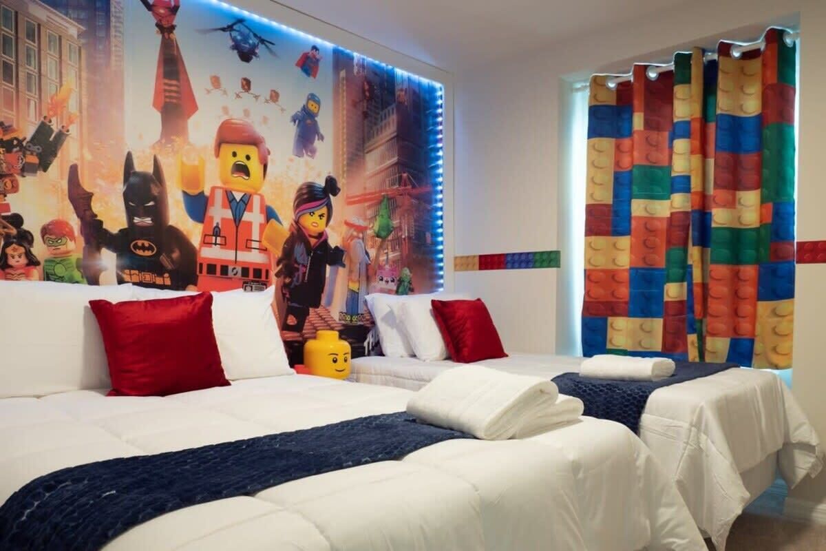 Une chambre d’hôtel avec deux lits, une fresque murale colorée sur le thème de LEGO et un rideau multicolore.