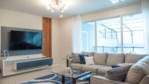 Ein modernes Wohnzimmer mit Flachbildfernseher, einer Couch, einem Couchtisch und einem großen Fenster.