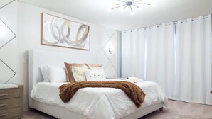 Ein modernes Schlafzimmer mit Bett, Nachttisch, Wandlampe und einem großen abstrakten Gemälde.