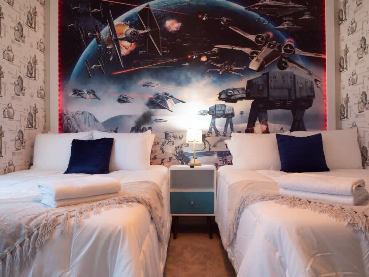 A bedroom with two beds, a nightstand, and a wall mural of space-themed artwork.