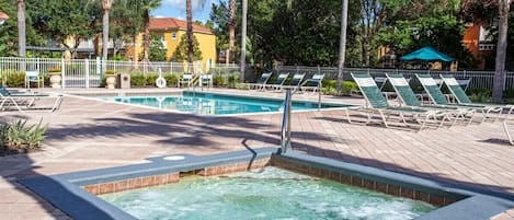 A pool area with lounge chairs, a hot tub, and a fenced poolside.