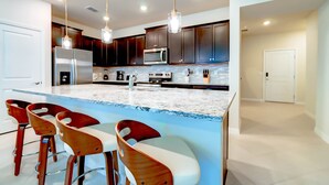 A modern kitchen with dark wooden cabinets, a stainless steel refrigerator, a built-in microwave, and a marble island with bar stools. - Luxurious Townhouse w/ Private Pool Near Attractions (Clermont)
