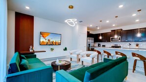 A modern living room with a sofa, coffee table, and a TV. There is a kitchen area with cabinets and a microwave. - Luxurious Townhouse w/ Private Pool Near Attractions (Clermont)
