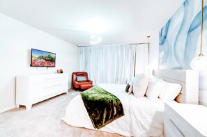 Ein modernes Hotelzimmer mit einem Bett, einem roten Sessel, einer weißen Kommode, einem Flachbildfernseher und einem großen Fenster mit Vorhängen.