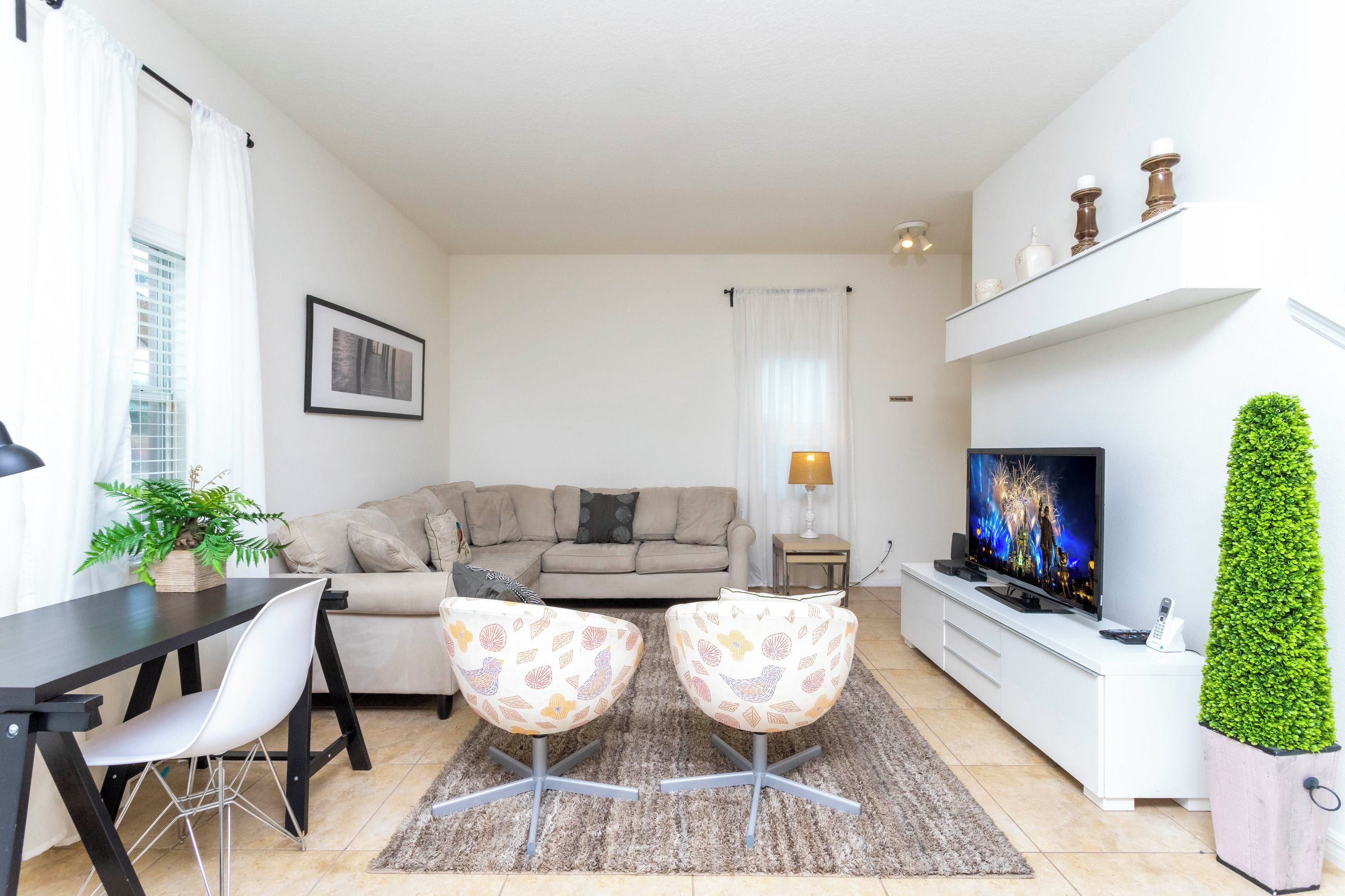 Un salon avec un canapé, deux fauteuils, un téléviseur, une plante et une table à manger.