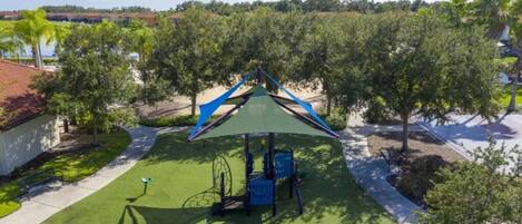 Une aire de jeux avec des balançoires et une structure d’escalade, entourée d’arbres et sous un ciel dégagé.
