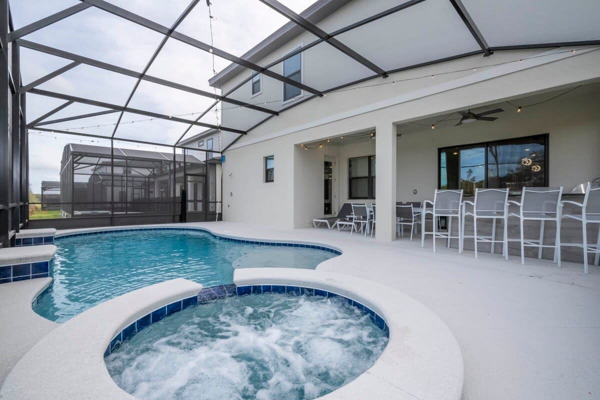 Una piscina interior amb un banyera d'hidromassatge, envoltada de cadires blanques i un tancament de vidre.