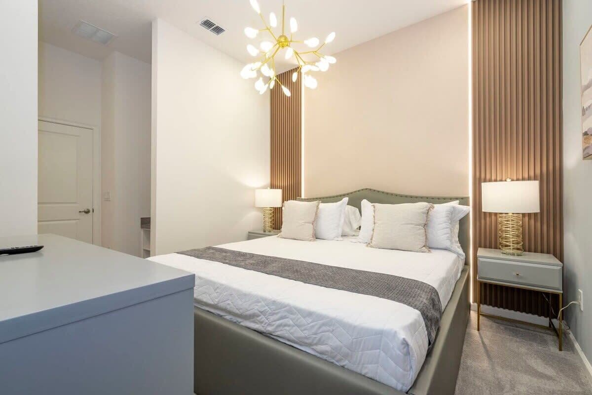 Quarto de hotel com cama, mesas de cabeceira, escrivaninha e um lustre moderno.