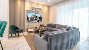 A modern living room with a grey sofa, a green armchair, a flat-screen TV, and a coffee table. - Luxury Townhouse w/ Private Pool Near Clubhouse (Davenport)