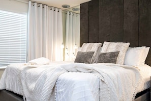 Ein Schlafzimmer mit Bett, Vorhängen und einer dunkel gestrichenen Wand.
