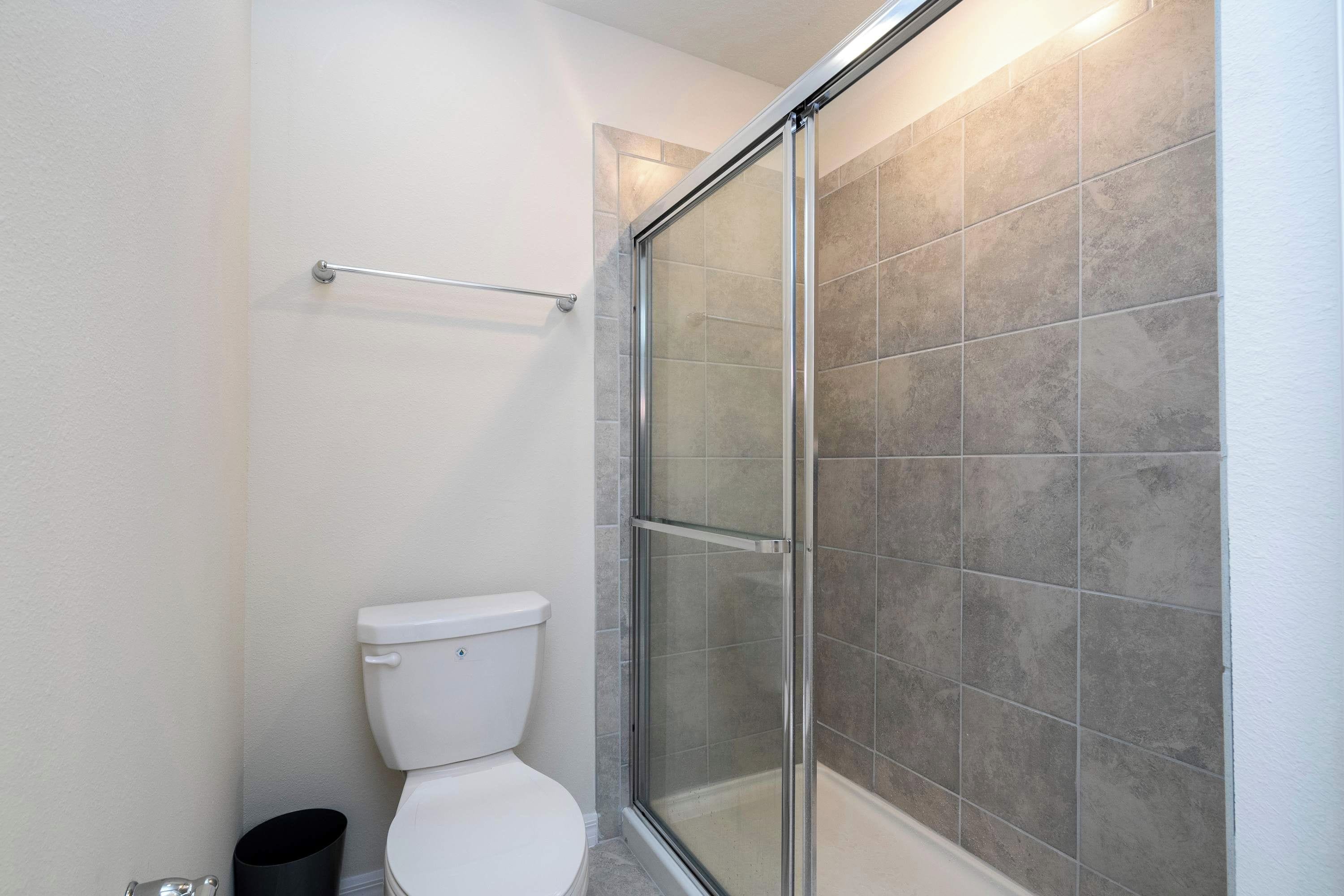 A bathroom with a toilet, a glass shower enclosure, and a tiled wall.