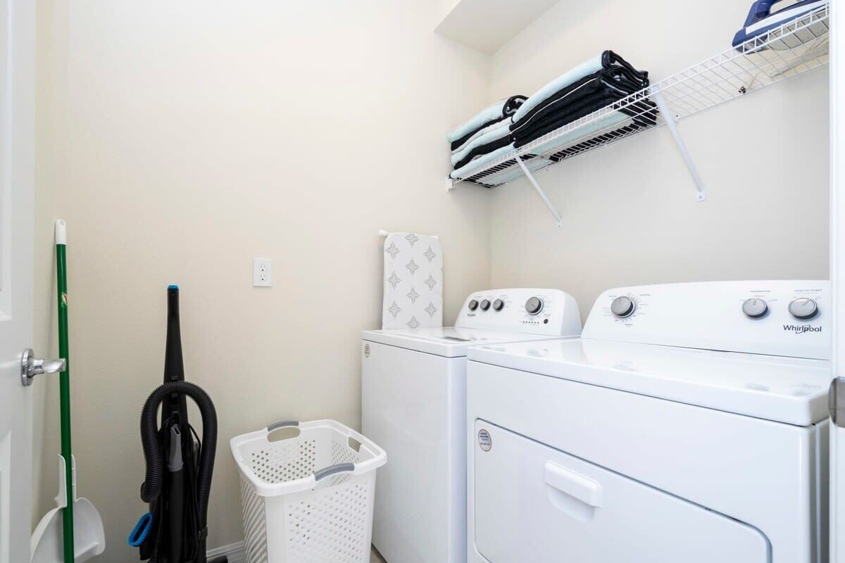 A laundry area with a stacked washer and dryer, a drying rack, a vacuum cleaner, and a laundry basket.