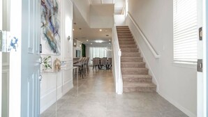 A hallway with a staircase, a dining area with chairs and a table, and a decorative wall piece. - Family-friendly Resort Home With Private Pool & Game Room (Davenport)