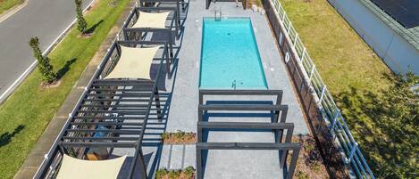 Una piscina en la azotea con zonas de estar a la sombra cercanas y vistas despejadas de la calle circundante.