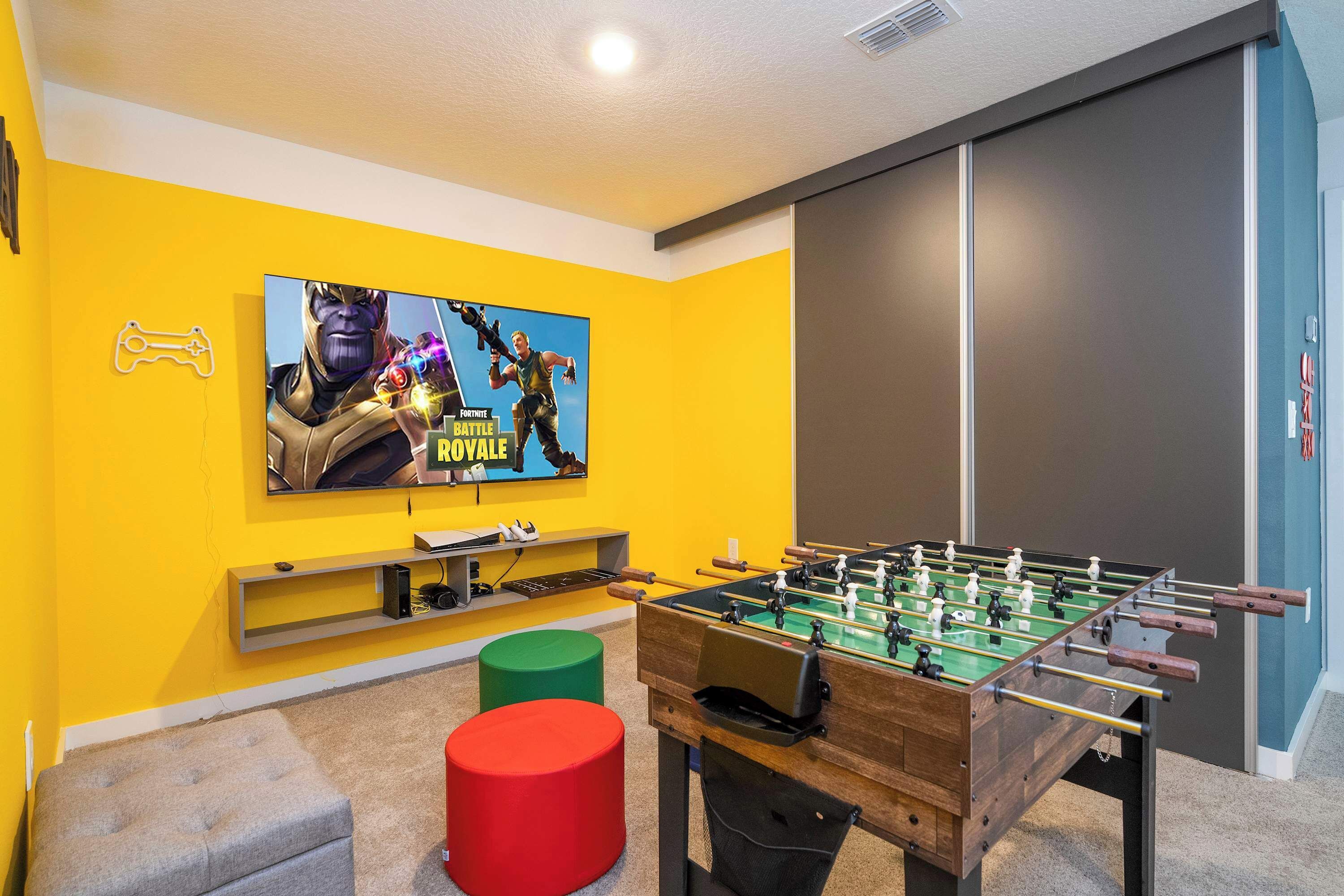 A room with a foosball table, a TV displaying a game, and a colorful wall.