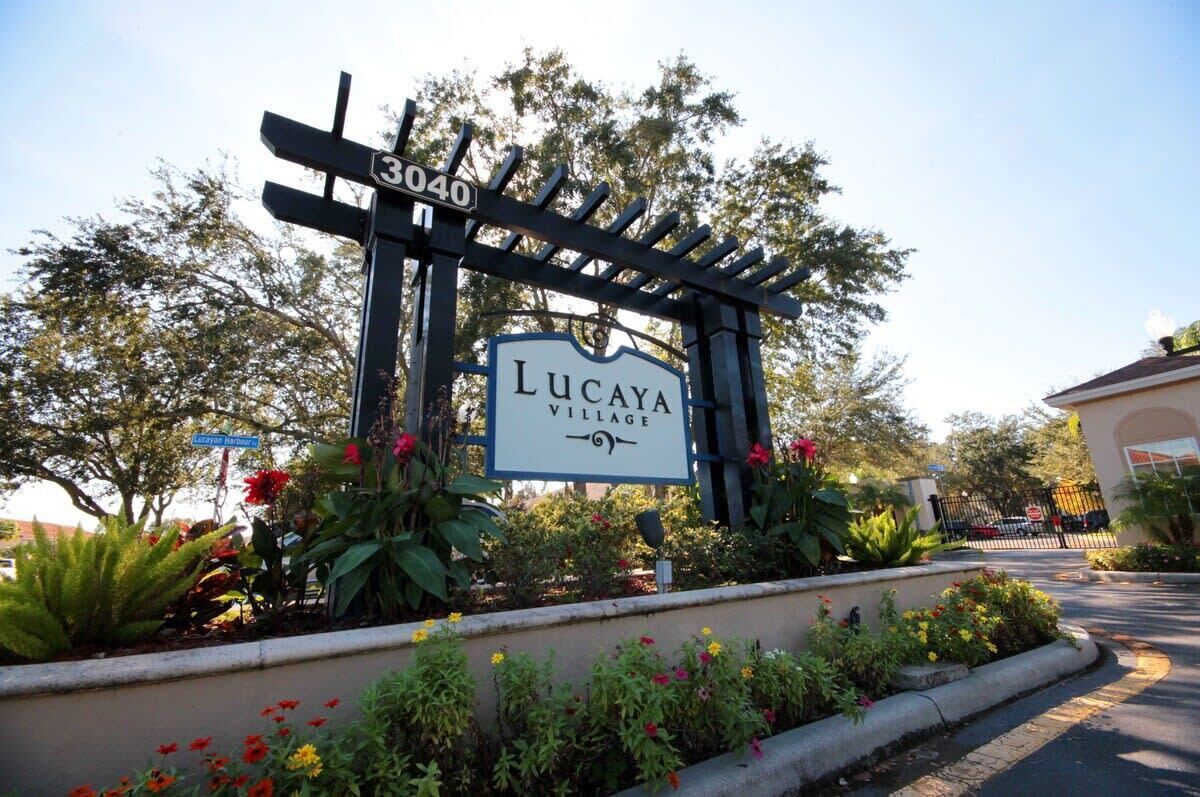 A gated entrance with a sign for Lucaya Village, surrounded by lush greenery and flowering plants.