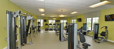 Ein Fitnessraum mit verschiedenen Trainingsgeräten, einem großen Spiegel und einem Fenster mit Jalousien.