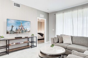 Ein modernes Wohnzimmer mit einem grauen Sofa, einem runden Couchtisch und einem an einer gestreiften Wand montierten Fernseher.