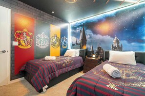 Ein Zimmer mit zwei Betten, jeweils mit einer rot-blauen, gestreiften Tagesdecke mit Wappenmuster. Die Wände sind mit einem Wandgemälde eines Schlosses und eines Sternenhimmels verziert.