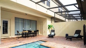 A swimming pool with a tiled edge, a covered patio area with a table and chairs, and a lounge chair. - Windsor Westside Resort Townhouse w/ Pool & Fast Wifi (Kissimmee)