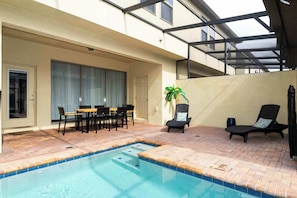 Ein Swimmingpool mit Fliesenrand, eine überdachte Terrasse mit Tisch und Stühlen sowie eine Liege.