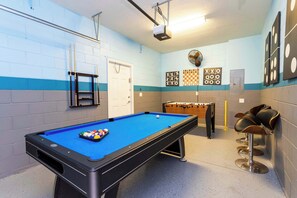 Ein Billardtisch mit Kugeln, ein Kicker und ein weiterer Billardtisch in einem Raum mit blauen und weißen Wänden.