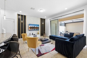 A modern living room with a cityscape painting, a dining area with a round table, and a balcony with chairs.