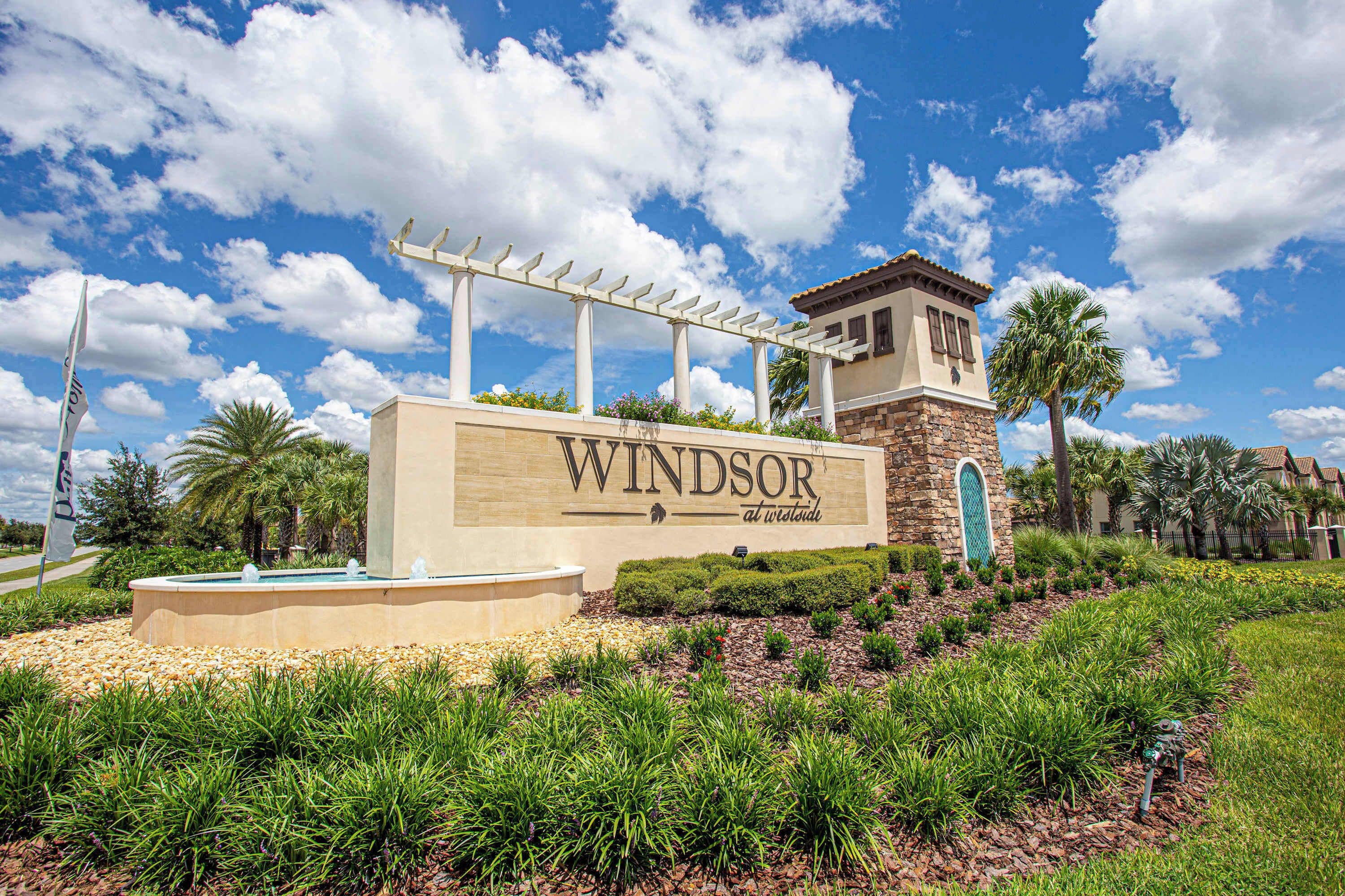 A sign for 'Windsor at Worldwide' with a pergola, palm trees, and a stone tower.