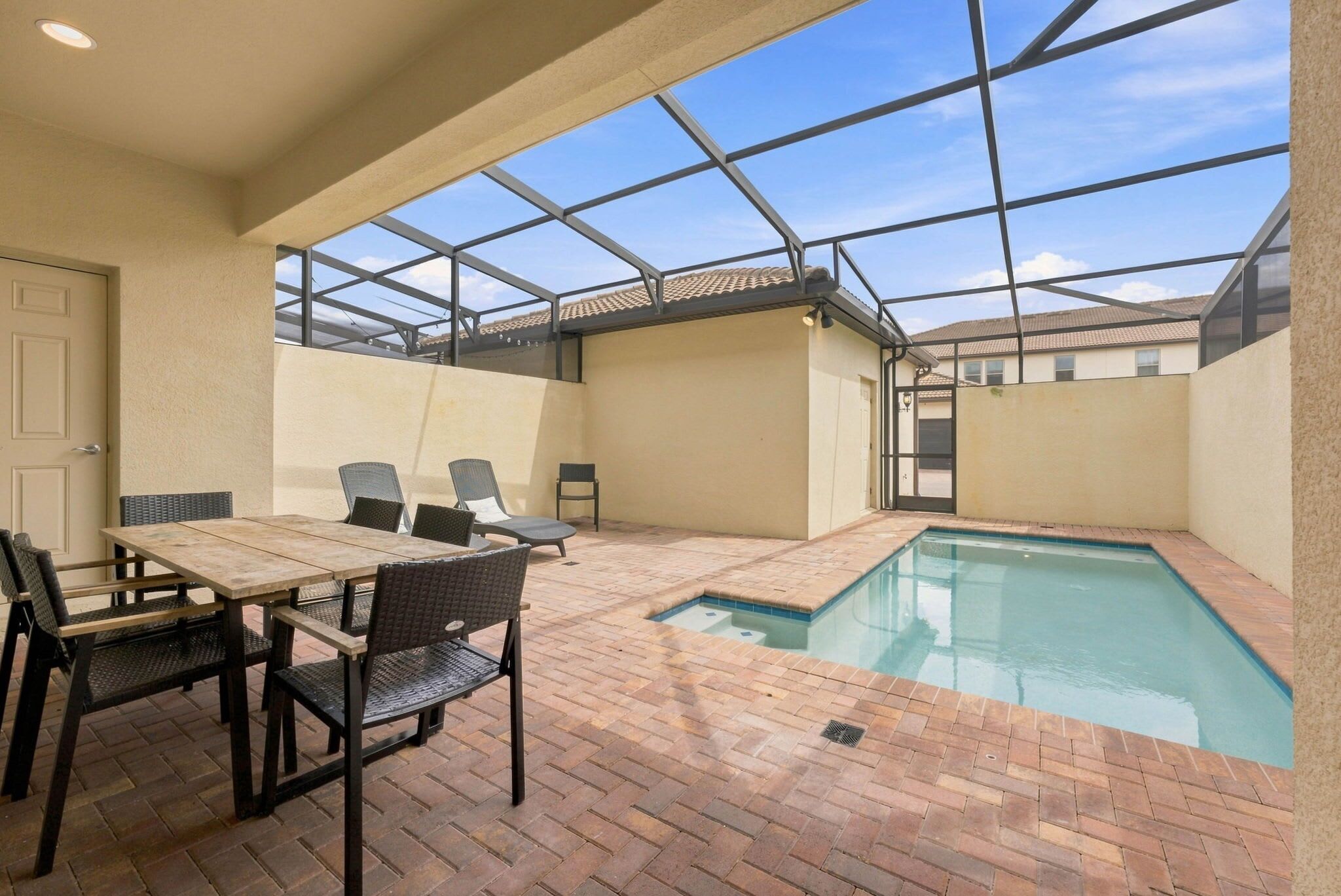 An outdoor pool area with a table and chairs, a glass ceiling, and a brick floor.