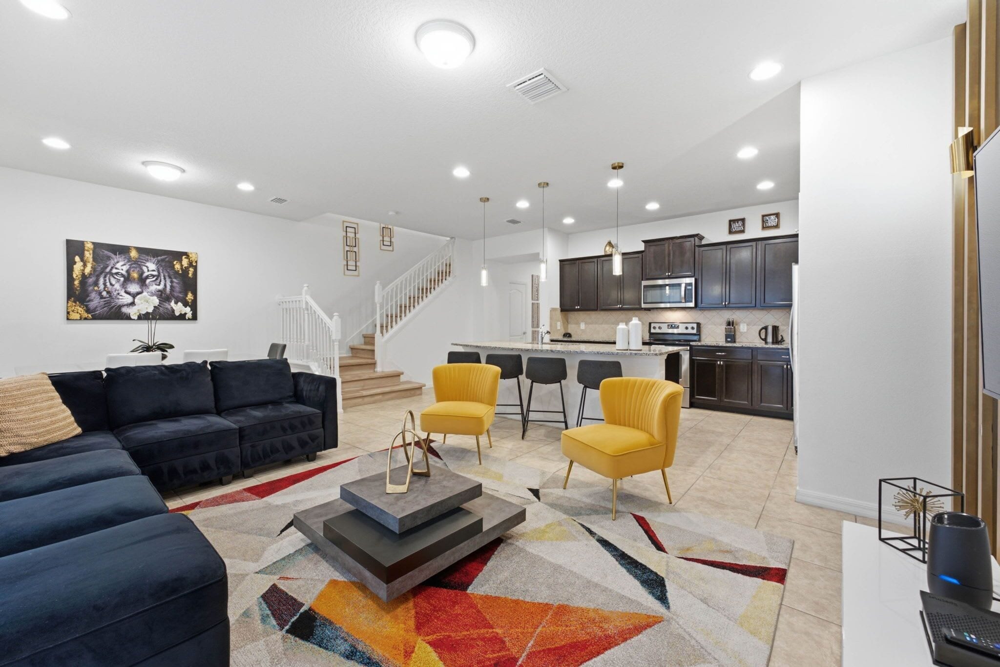 A modern living room with a sofa, chairs, a coffee table, and a staircase leading to the kitchen.