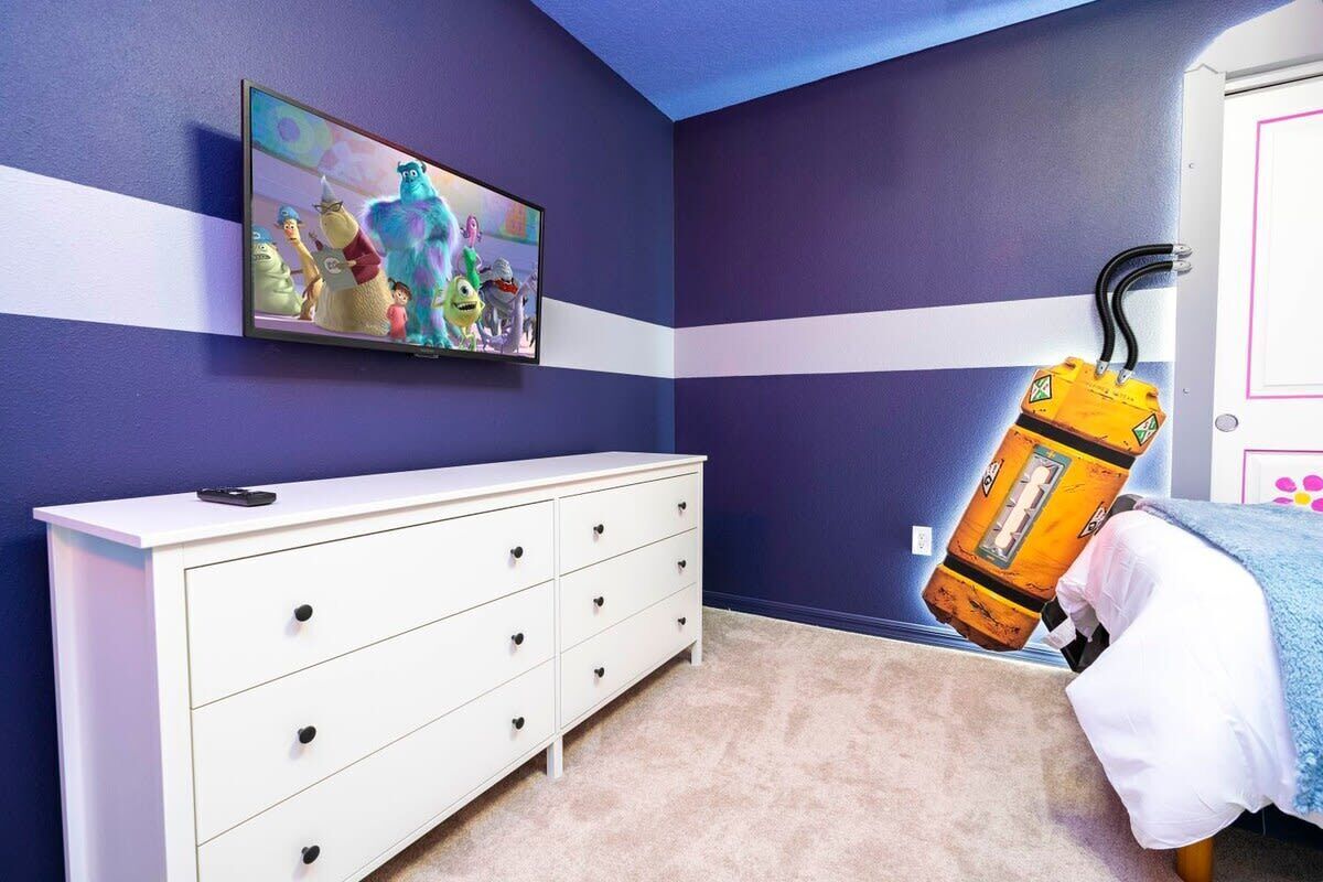 A bedroom with a bed, a white dresser, a painting on the wall, and a door.