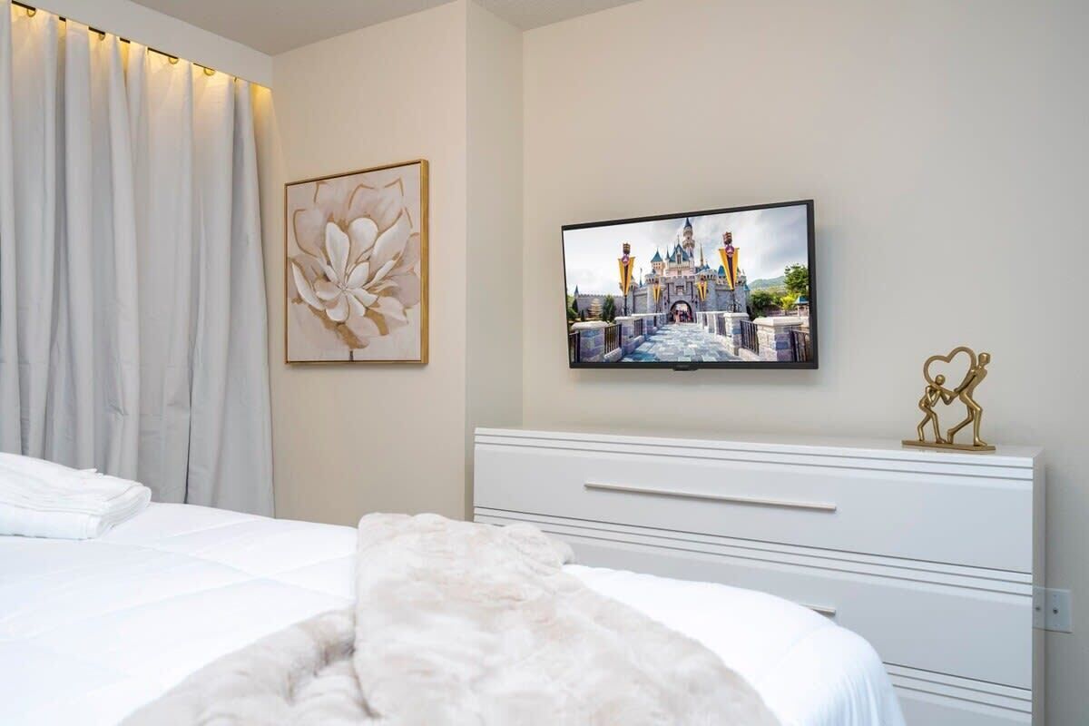 A bedroom with a bed, a TV mounted on the wall, and a decorative piece above the TV.