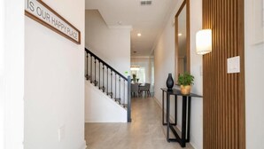 A hallway with a staircase, a sign that says 'IS OUR HAPPY PLACE', a console table with a plant, and a wooden panel wall. - Luxury Family Townhouse w/ Resort Pool at Storey Lake (Kissimmee)