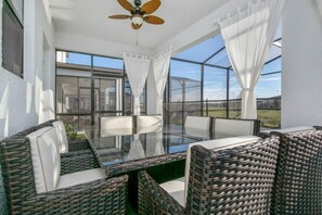 Eine sonnendurchflutete Terrasse mit Korbmöbeln, einem Glastisch und einem Deckenventilator.