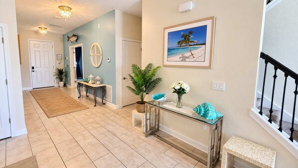 A hallway with a glass console table, a potted plant, and a framed picture of a beach scene. - Storey Lake Resort House w/ Cinema & Game Room! (Kissimmee)